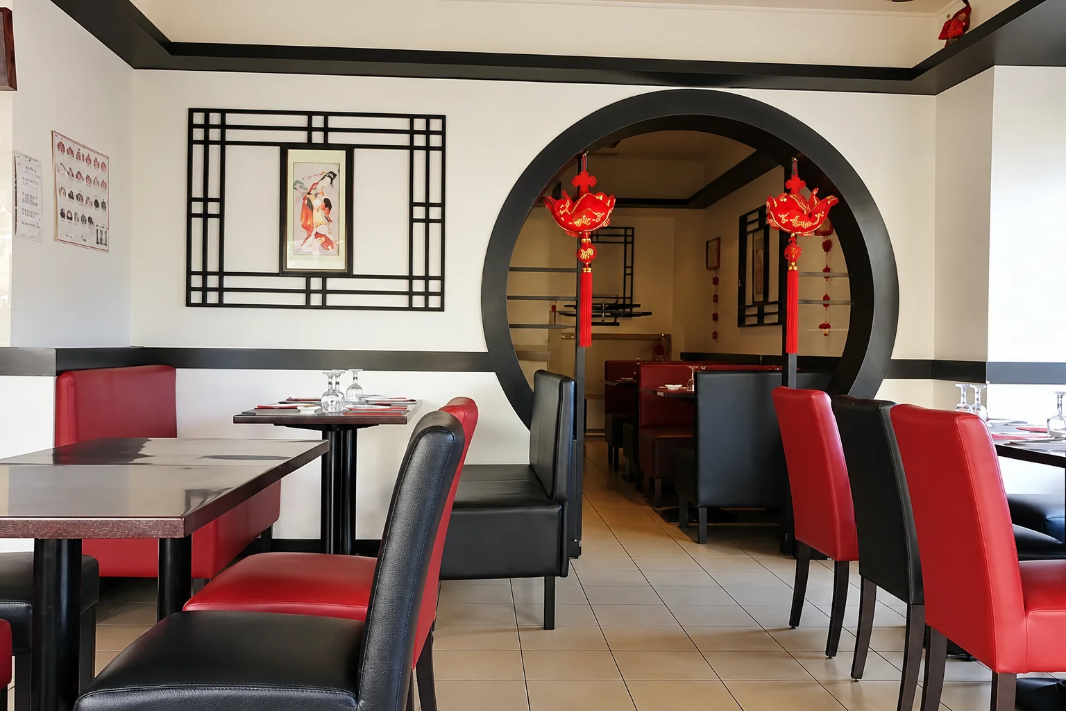 Salle avec porte ronde, lanternes rouges, tables noires et chaises rouges et noires.