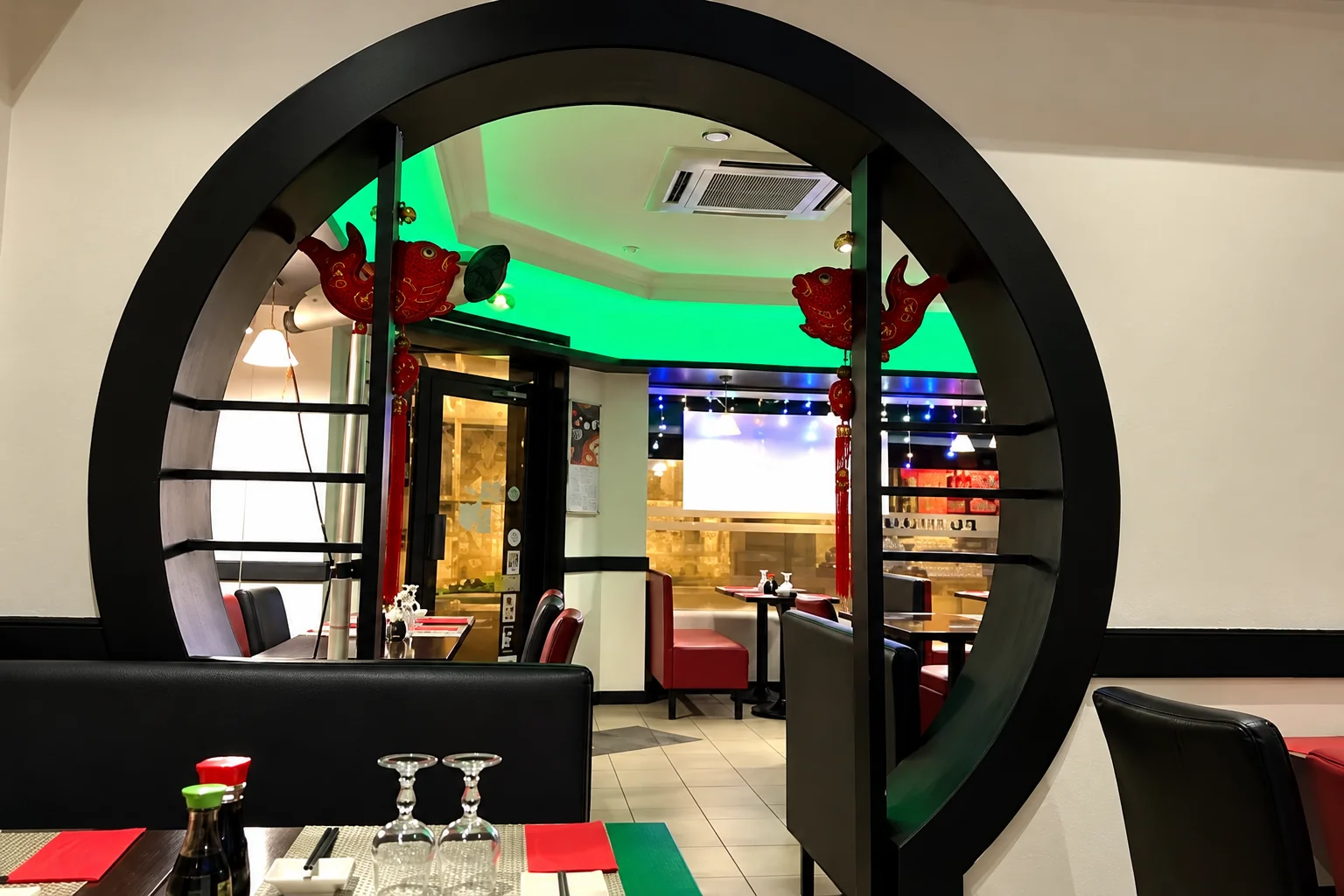 Porte ronde noire avec décorations rouges, salle éclairée en vert au fond, verres sur la table.