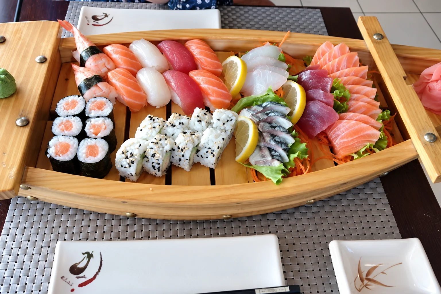 Bateau en bois avec sushi, makis, california et sashimi, posé sur une table.