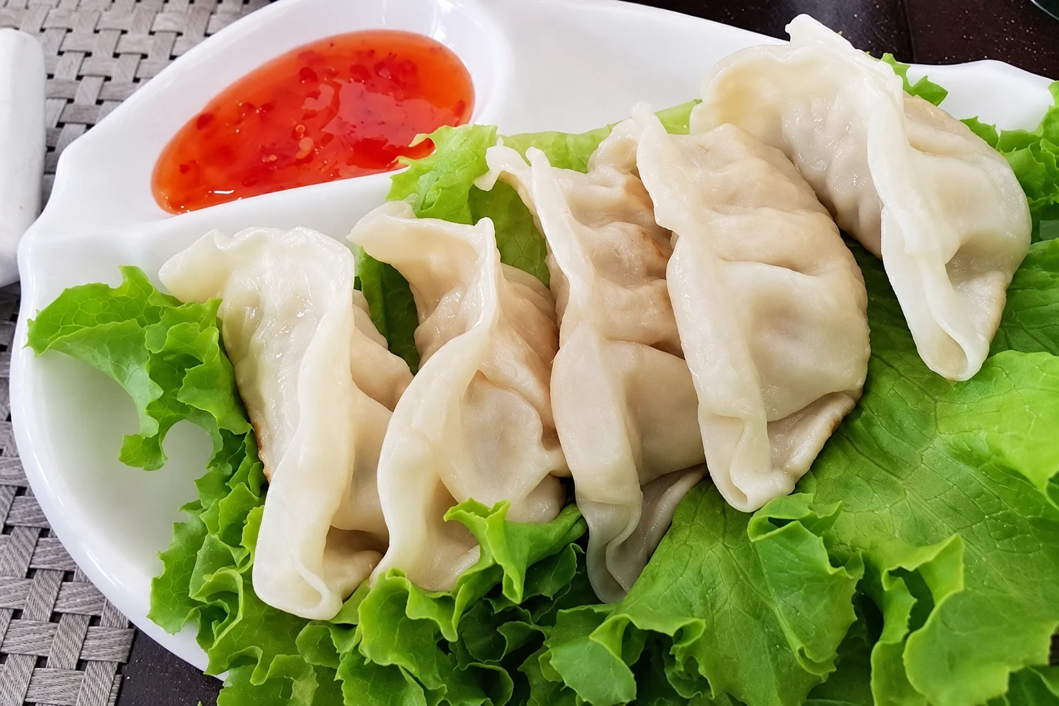 Raviolis sur des feuilles de salade, sauce rouge dans une coupelle, assiette blanche.